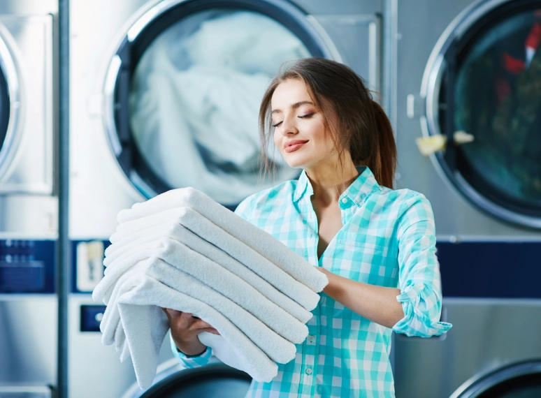 Woman holding folded laundry in laundromat.